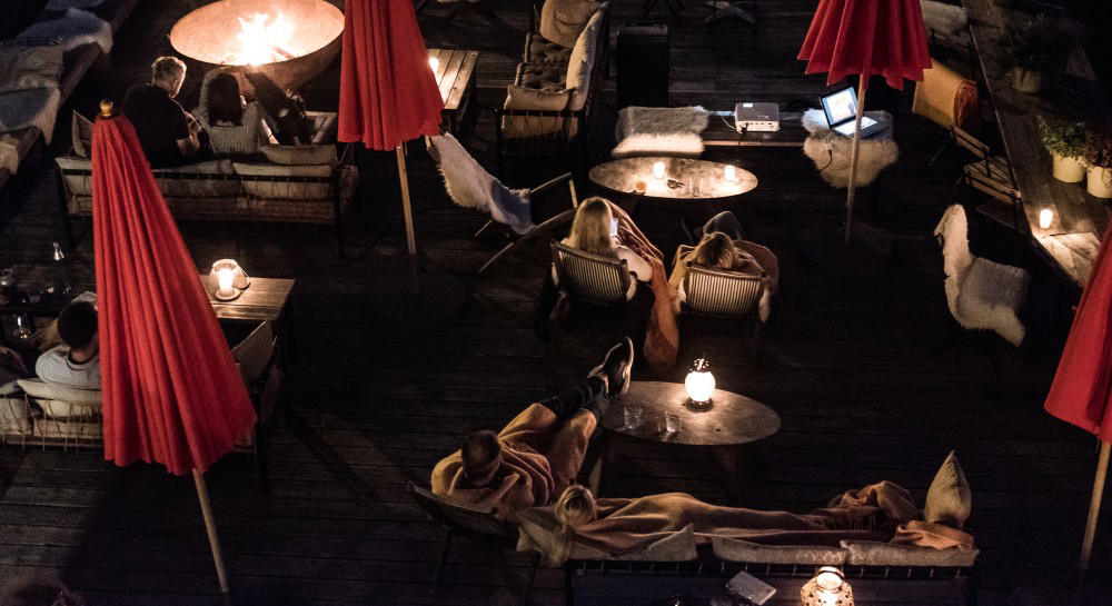 Obenansicht der Terrasse bei Nacht, Menschen sitze da eingedeckt bei Kerzenschein